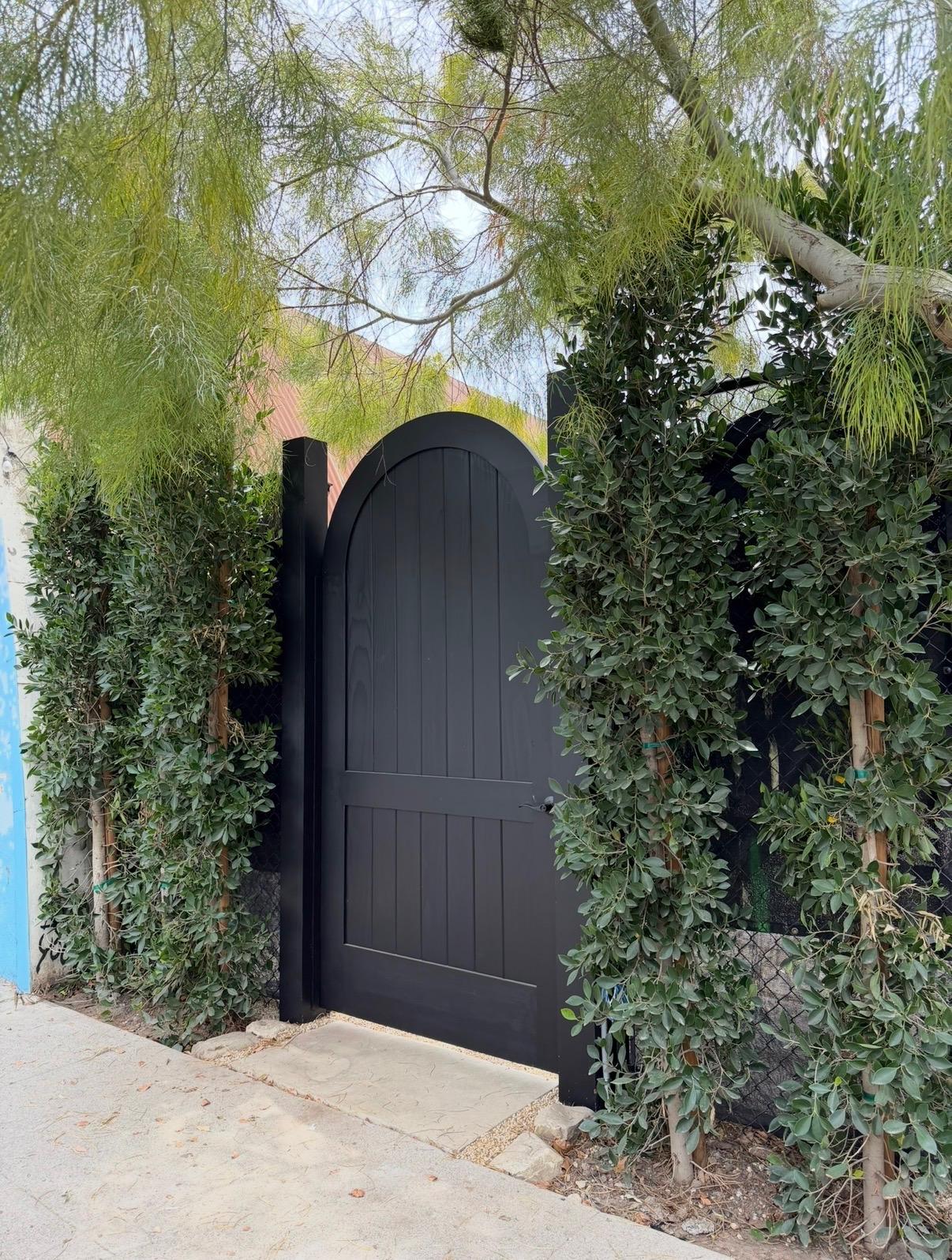 The black arched gate at the studio entrance, framed by greenery